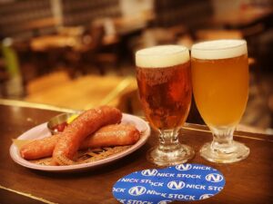 京都駅近くにある肉カフェ「NICK STOCK イオンモールKYOTO店」にて提供する極太ソーセージのグリルとクラフトビール2種（豊潤・シルクエール）のイメージ写真